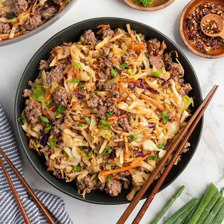 Egg roll in a bowl with ground beef, cabbage, carrots, and green onions served in a black bowl with chopsticks.