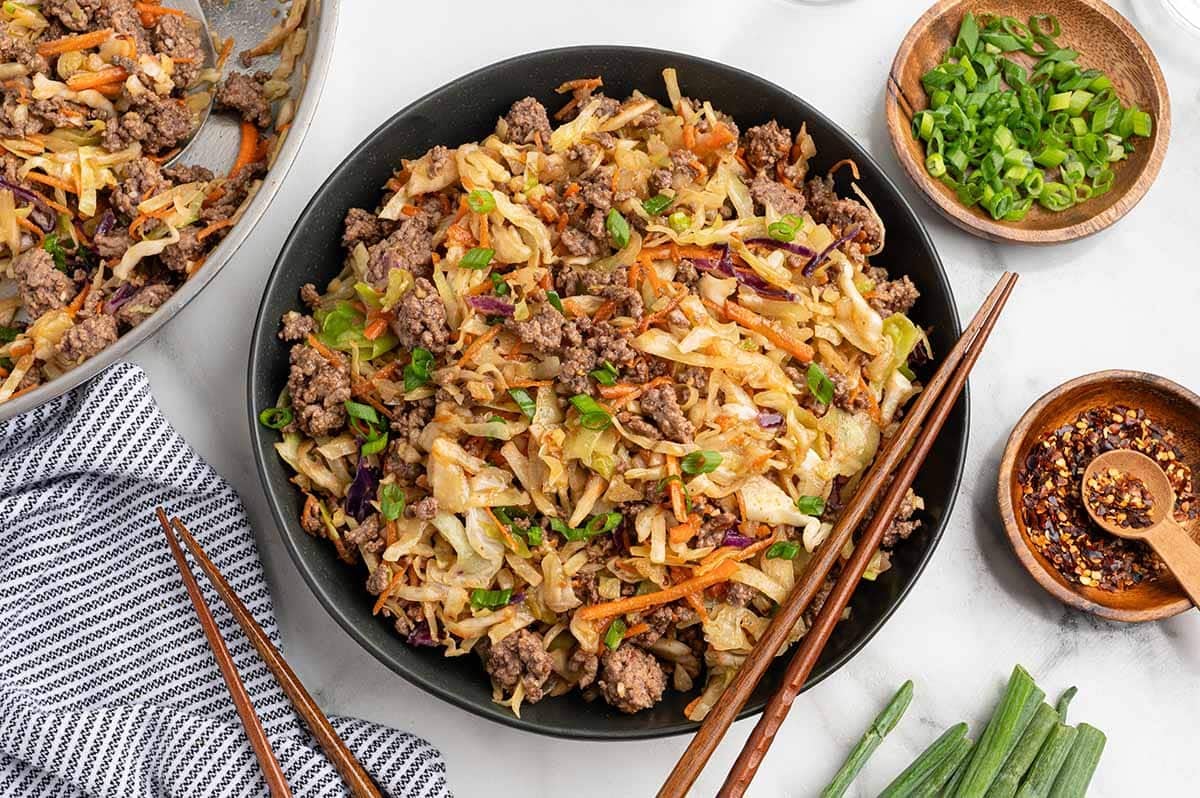 Egg roll in a bowl made with ground beef, cabbage, carrots, and green onions, served with chopsticks and garnished with green onions.