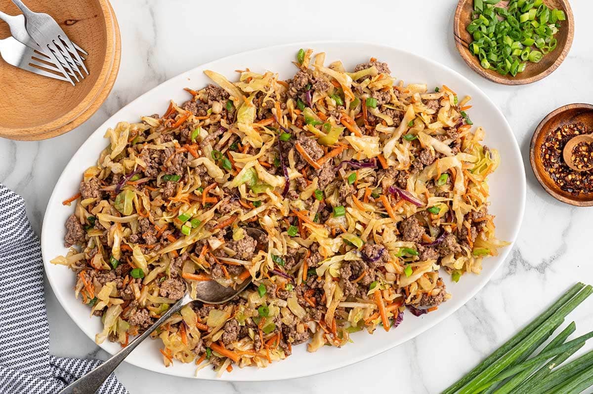 Egg roll in a bowl with ground beef, cabbage, carrots, and green onions served on a large platter.