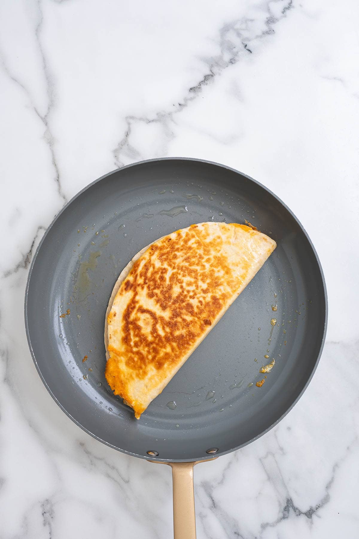 Golden brown folded chicken fajita quesadilla cooking in a skillet.