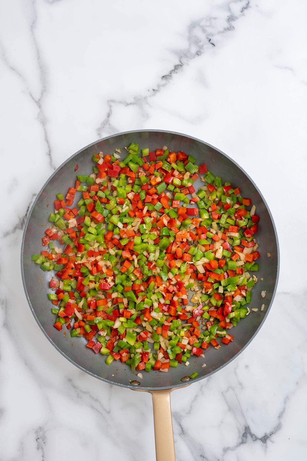 Diced red and green bell peppers and onions sautéing in a skillet.