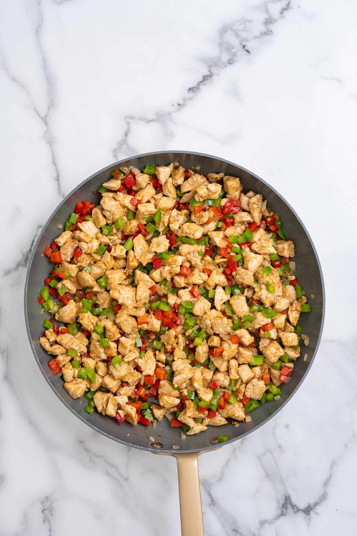 Cooked chicken mixed with sautéed bell peppers and onions in a skillet.