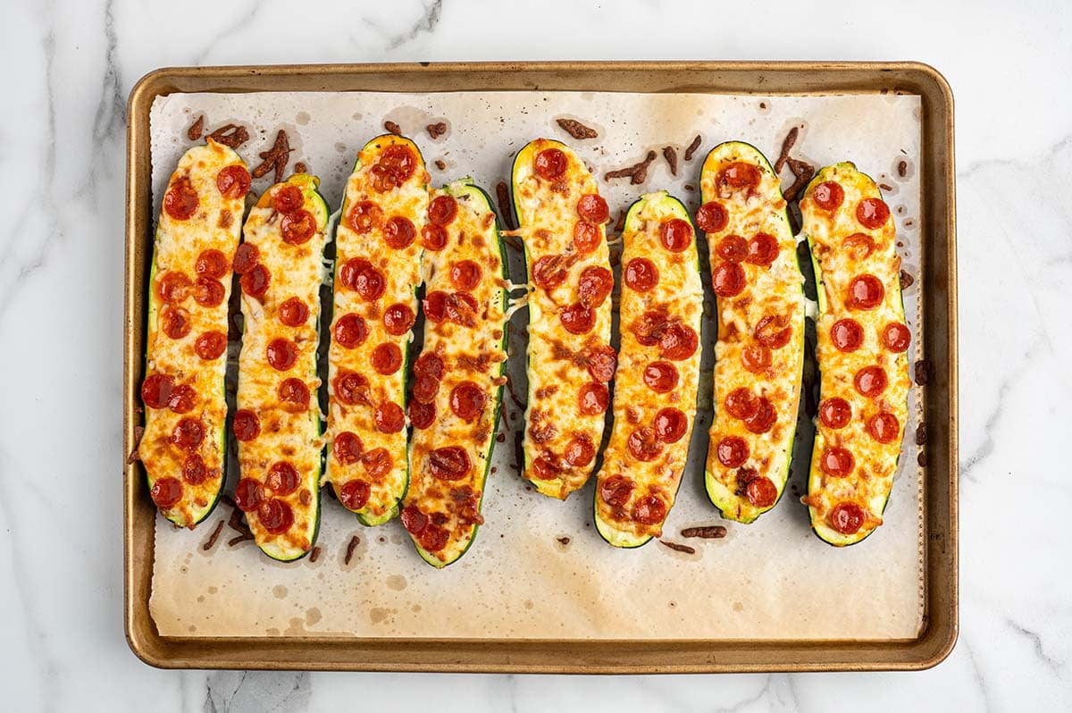 Baked zucchini pizza boats topped with melted mozzarella and crispy mini pepperoni slices, arranged on a parchment-lined baking sheet.
