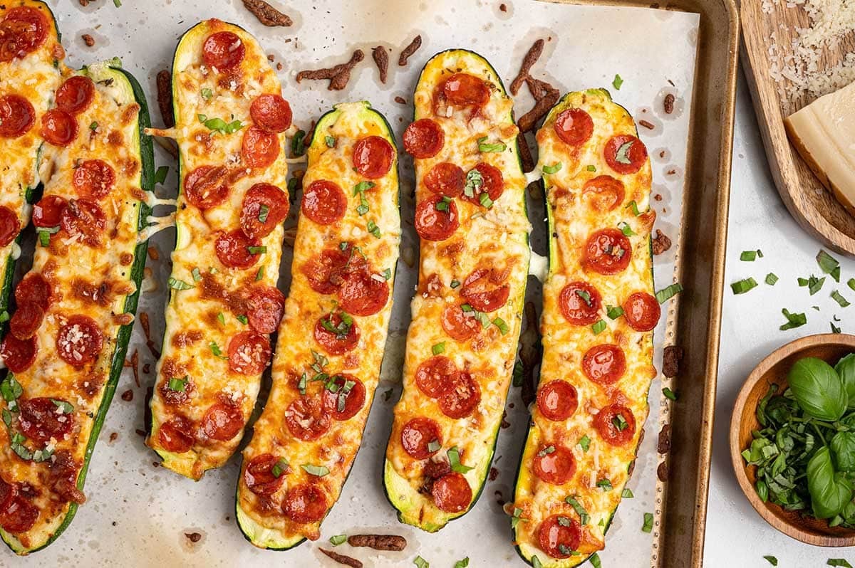 Pizza Zucchini Boats topped with melted mozzarella, mini pepperoni, and fresh basil on a parchment-lined baking sheet.