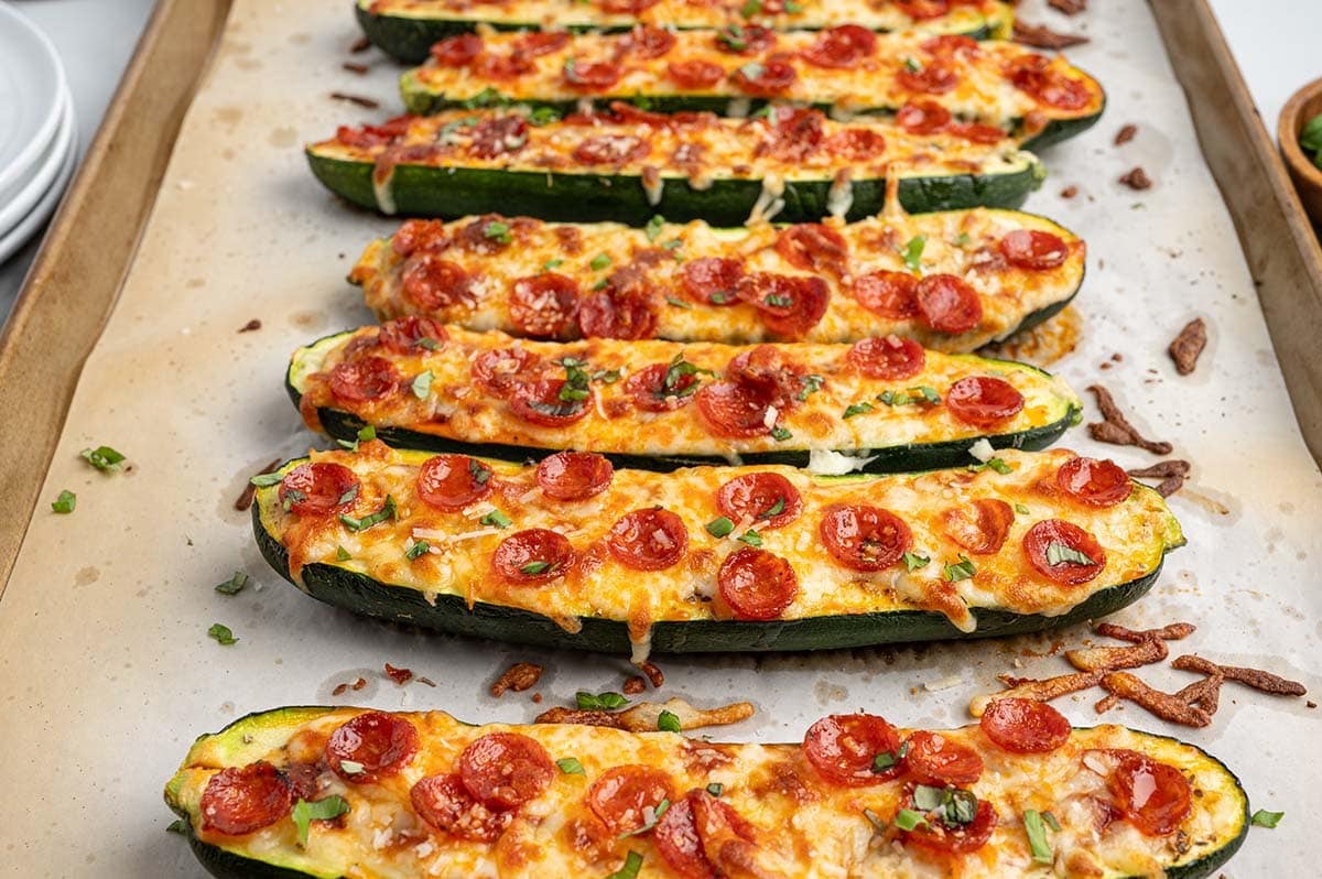 Pizza zucchini boats topped with melted cheese, mini pepperoni, and fresh basil on a baking sheet.