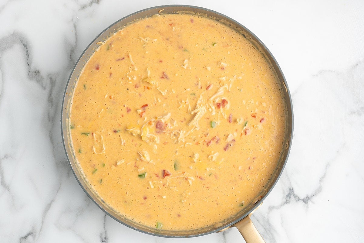 Creamy cheese sauce with shredded chicken and tomatoes simmering in a skillet.