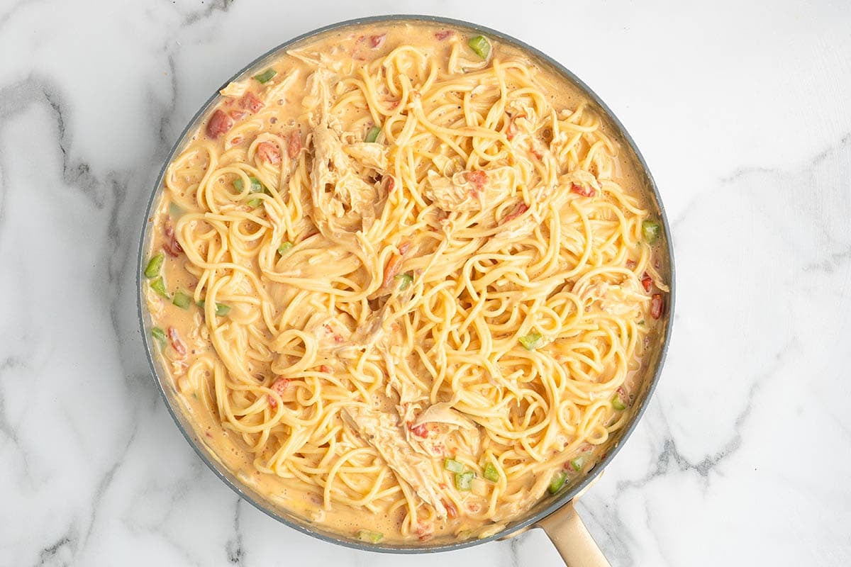 Spaghetti tossed with creamy chicken and tomato sauce in a skillet.