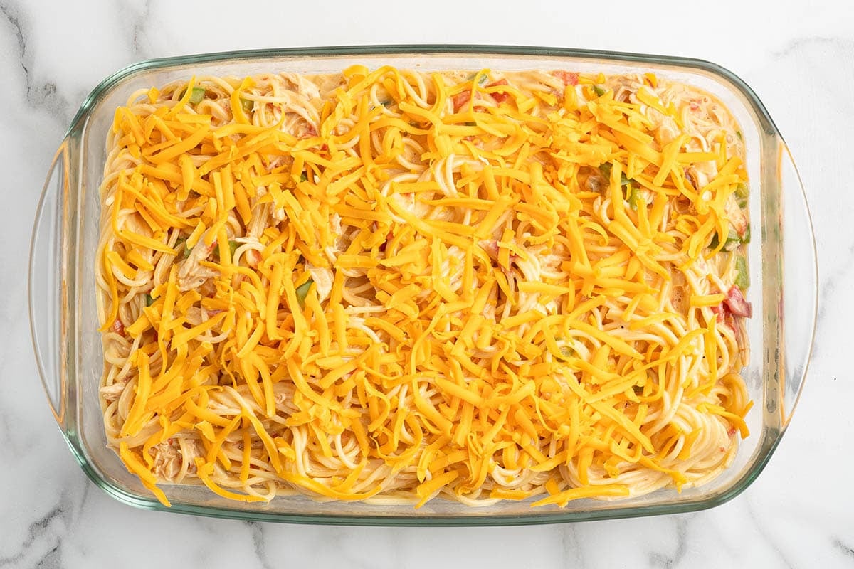 Chicken spaghetti casserole topped with shredded cheddar before baking.