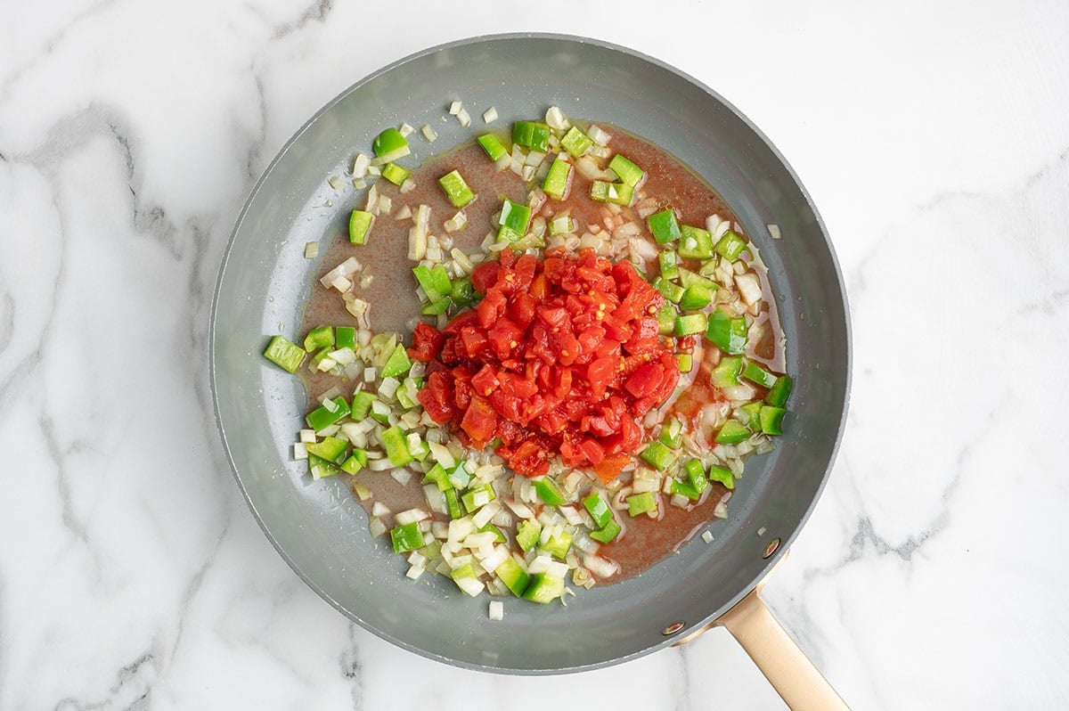 Diced tomatoes, green pepper, and onion cooking together in a skillet.