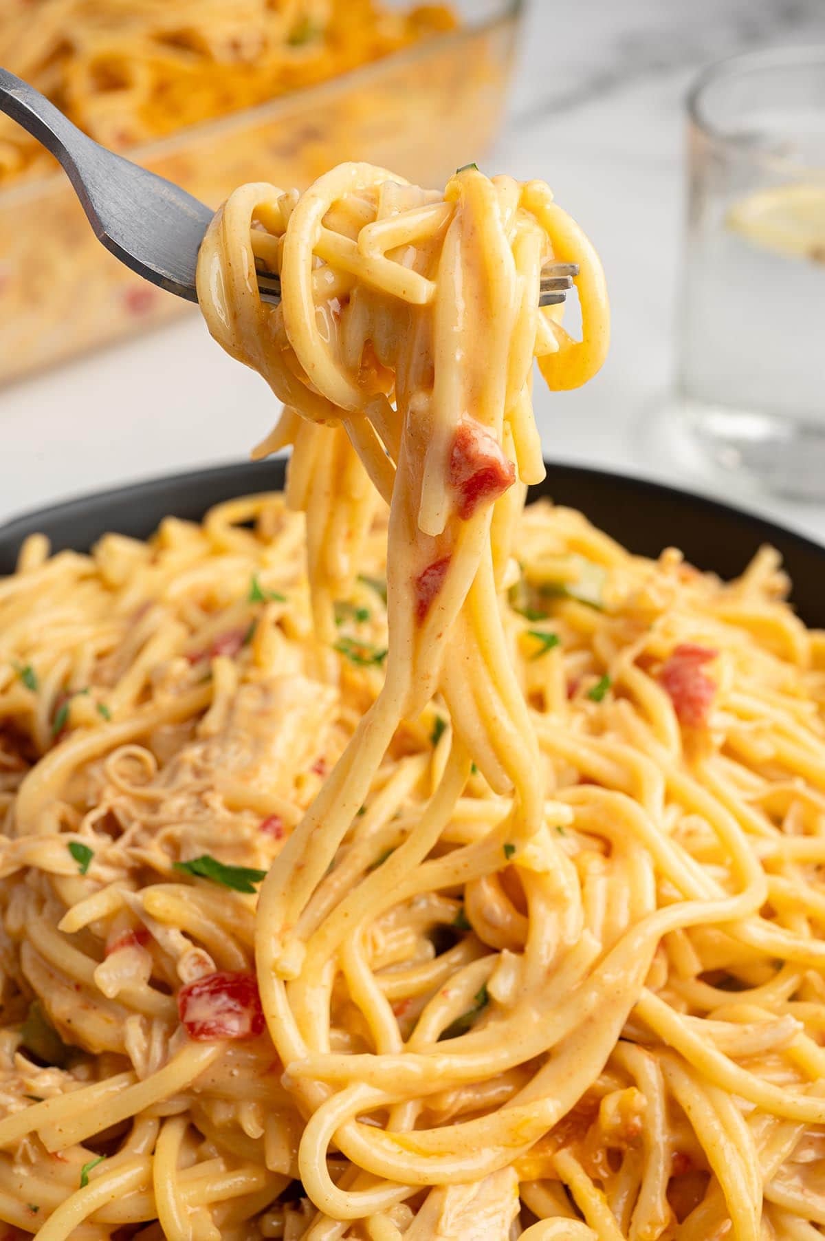 Fork twirling creamy Rotel chicken spaghetti above a bowl of the pasta.