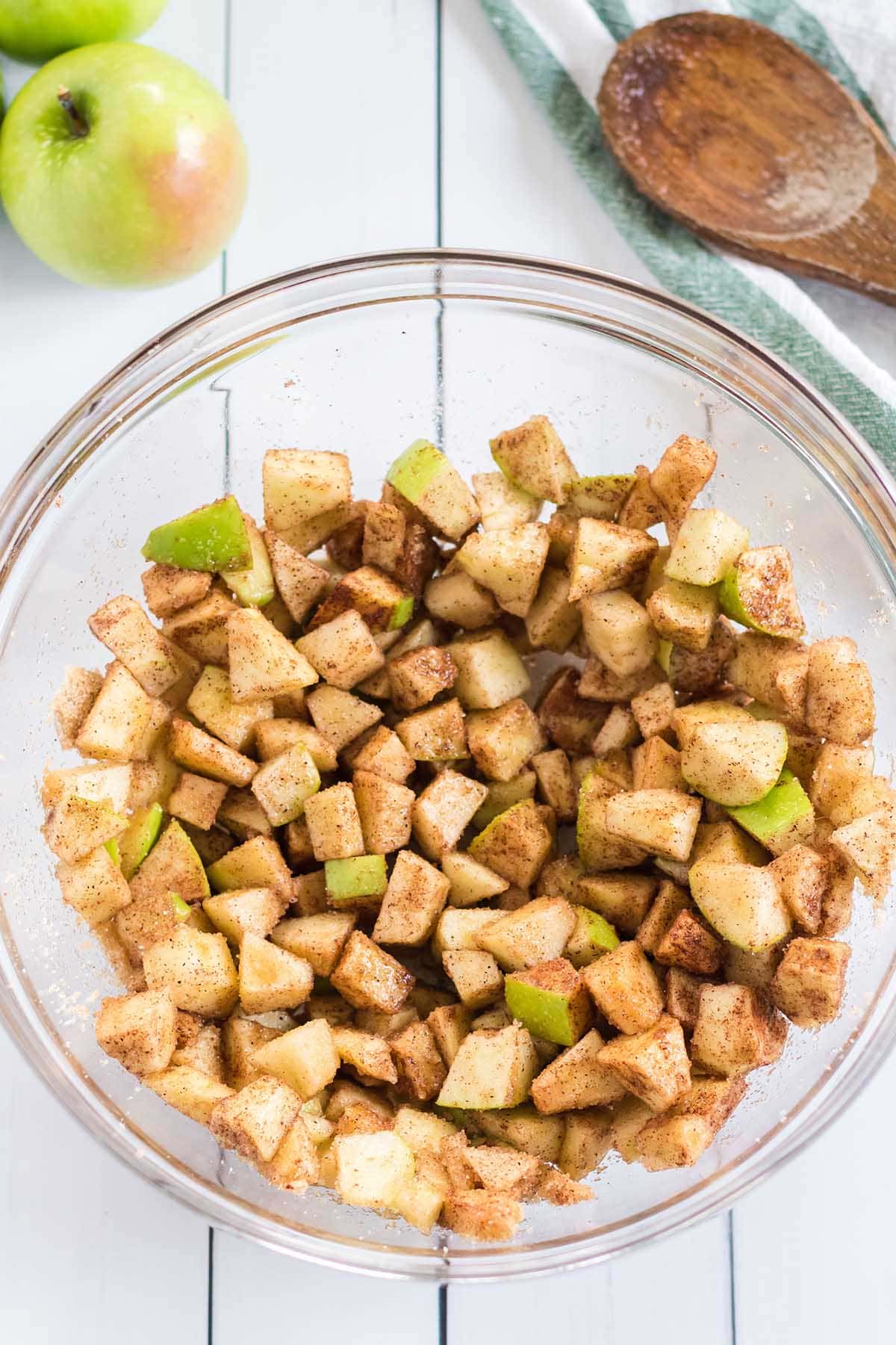 Chopped apples coated with cinnamon and sugar in a glass mixing bowl.