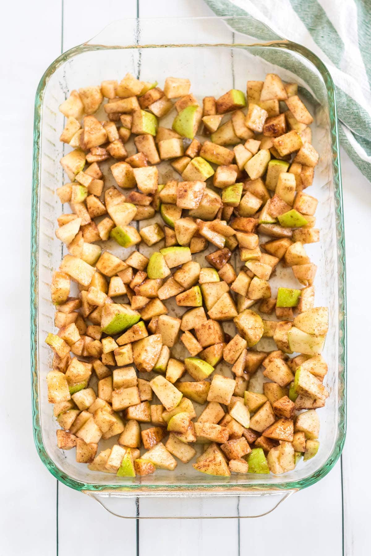Cinnamon coated chopped apples spread evenly in a glass baking dish.