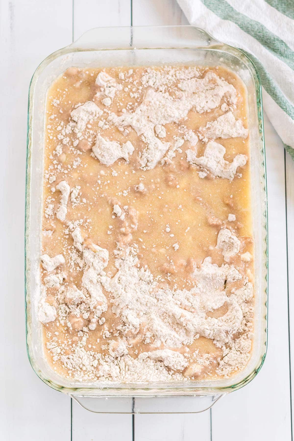Unbaked apple dump cake with cake mix and butter in a glass baking dish.