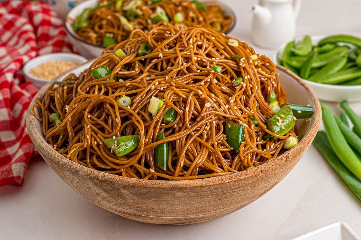Asian Noodle Salad with sesame-soy dressed noodles, cucumber, green onions, and sesame seeds in a large wooden bowl.