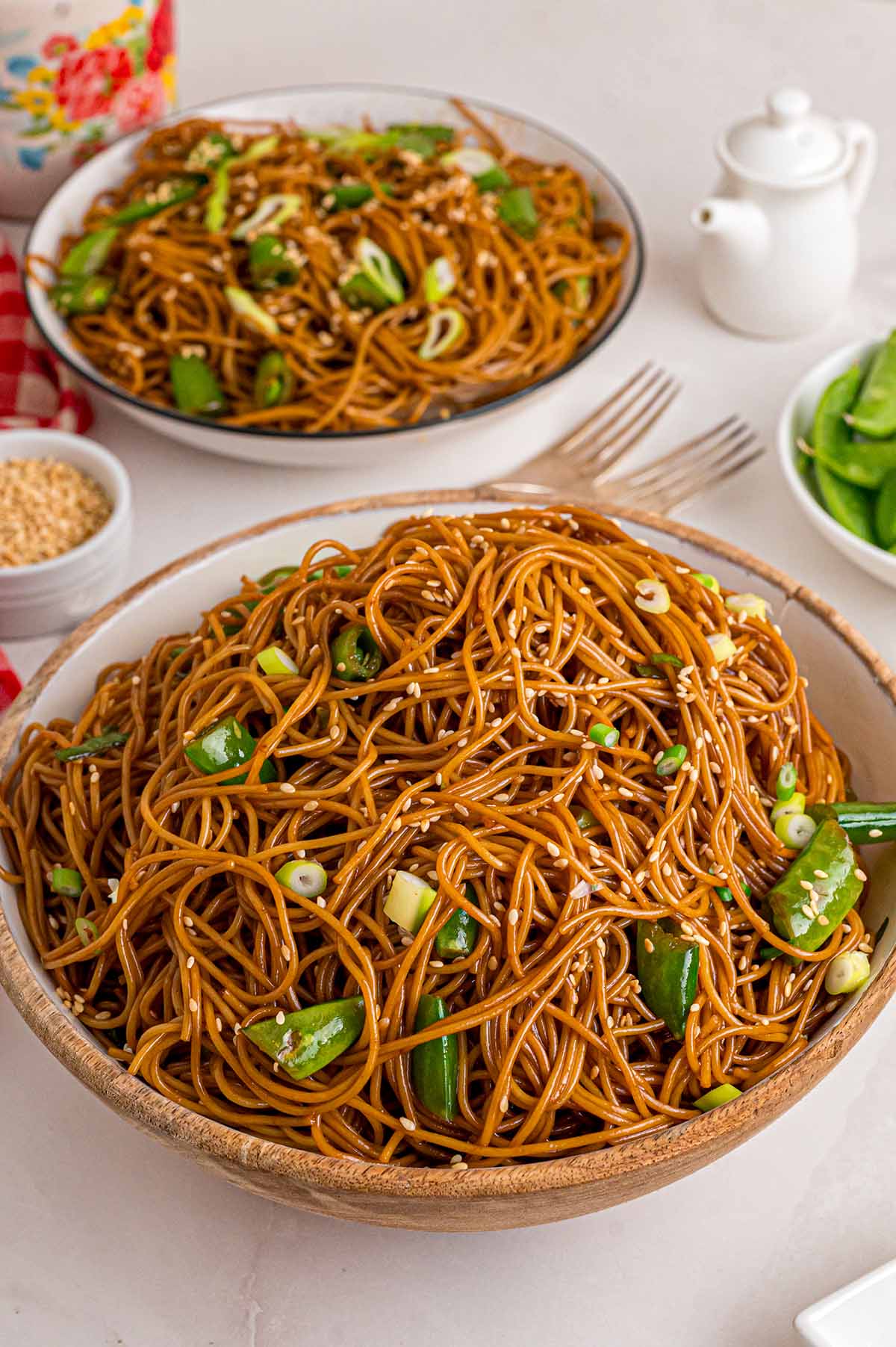 Asian Noodle Salad with sesame-soy dressed noodles, cucumber, green onions, and sesame seeds in a wooden bowl, with a second serving in a plate behind it.