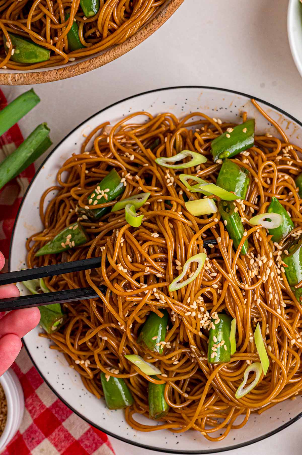 Overhead view of Asian Noodle Salad with cucumber, green onions, and sesame seeds being picked up with chopsticks from a speckled bowl.