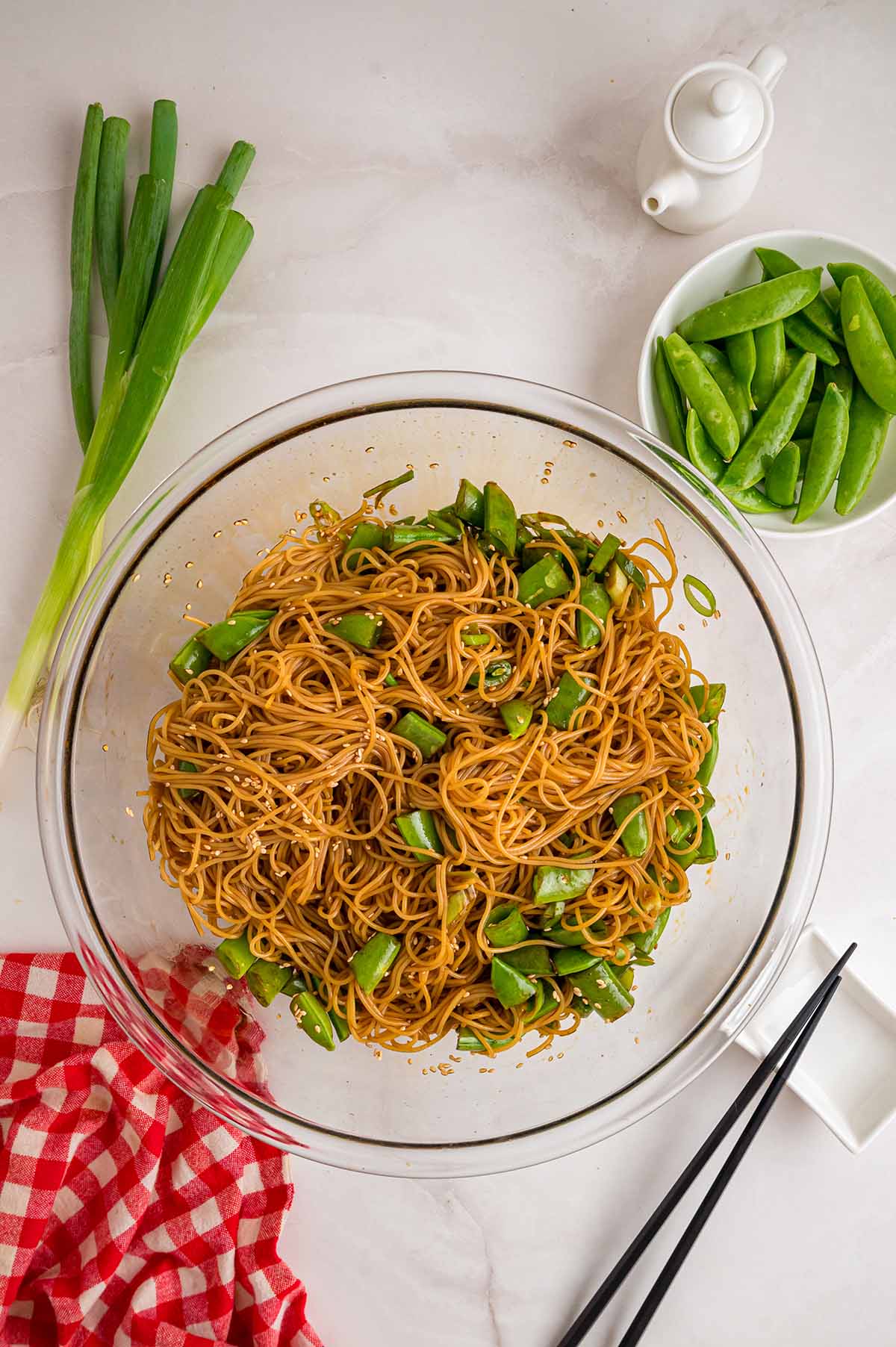 Asian noodle salad tossed with snap peas in a glass bowl.