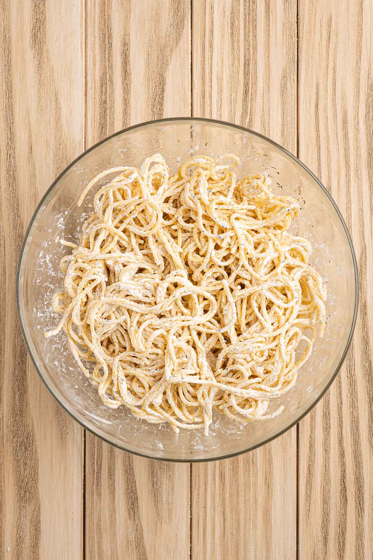 Spaghetti coated with a creamy cheese mixture in a glass bowl.