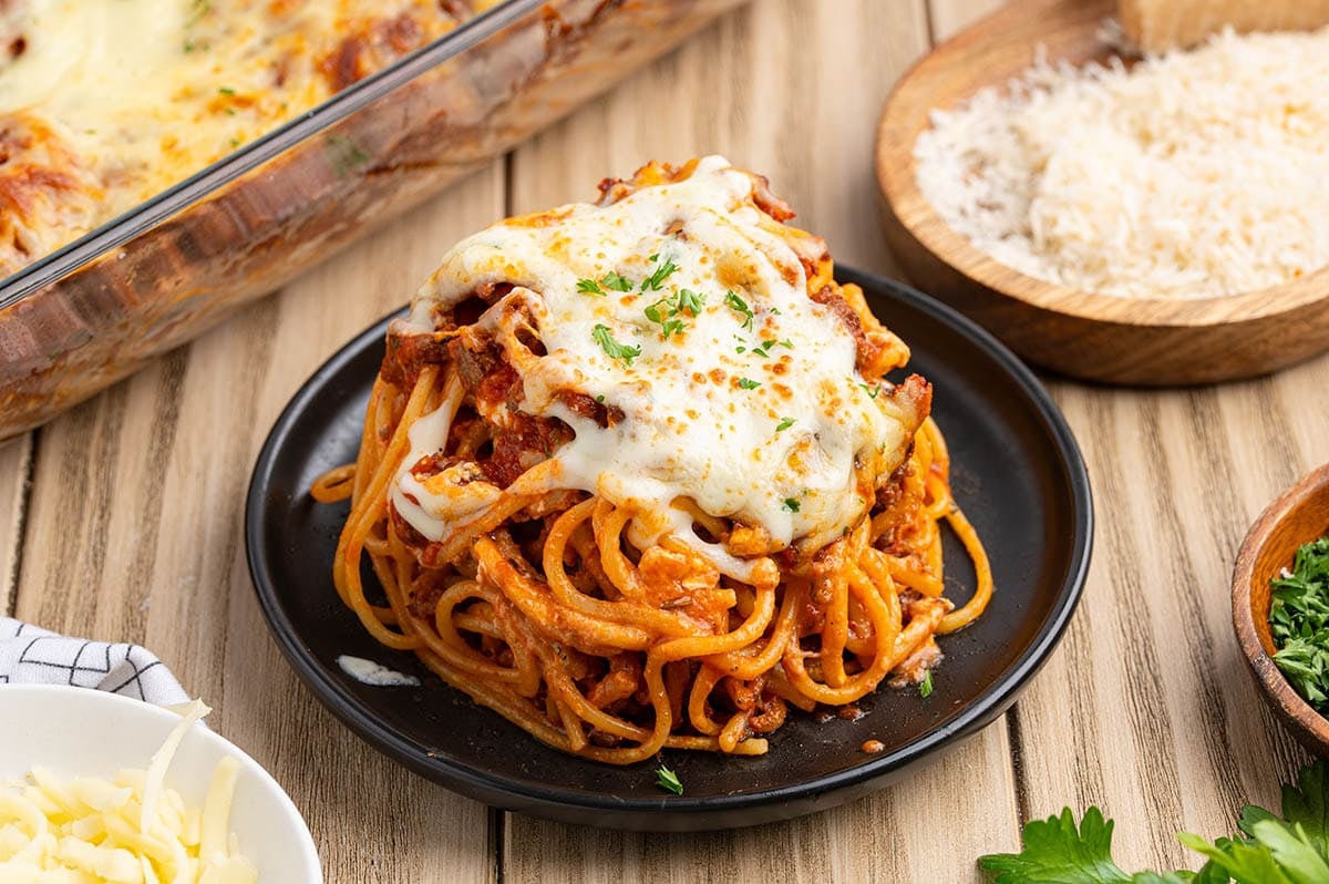 Slice of cheesy baked spaghetti topped with meat sauce and melted mozzarella.