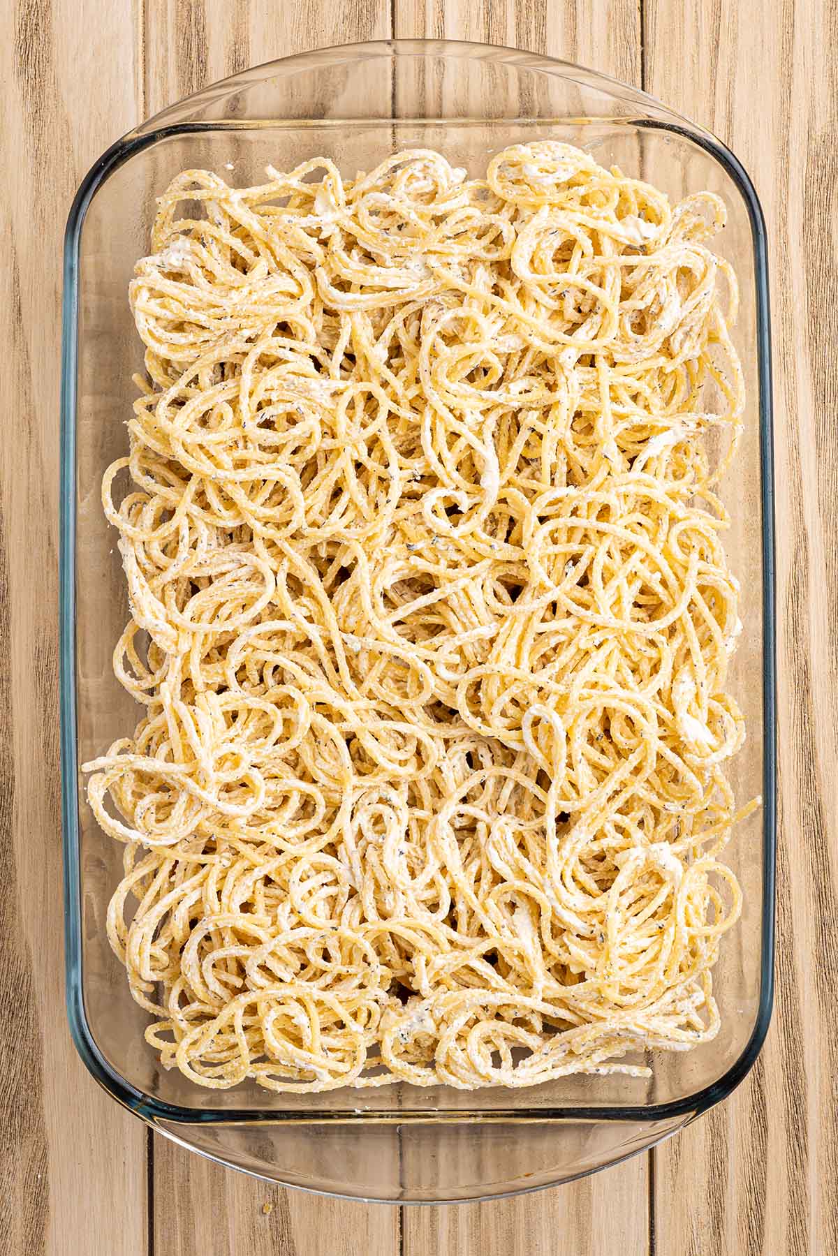 Cream cheese coated spaghetti spread evenly in a baking dish.