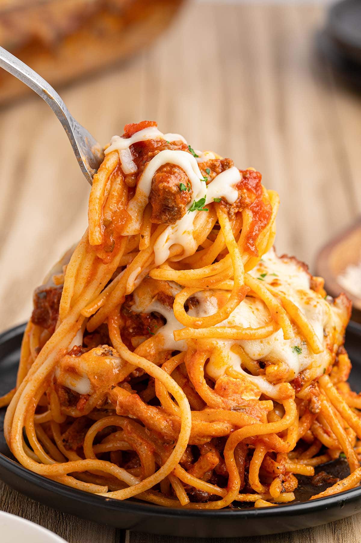 Fork lifting a bite of cheesy baked spaghetti with meat sauce.