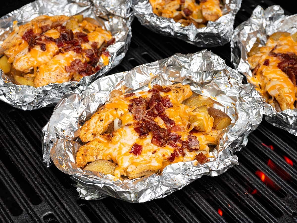 Cheesy bacon chicken foil packets cooking on the grill with crispy potatoes.