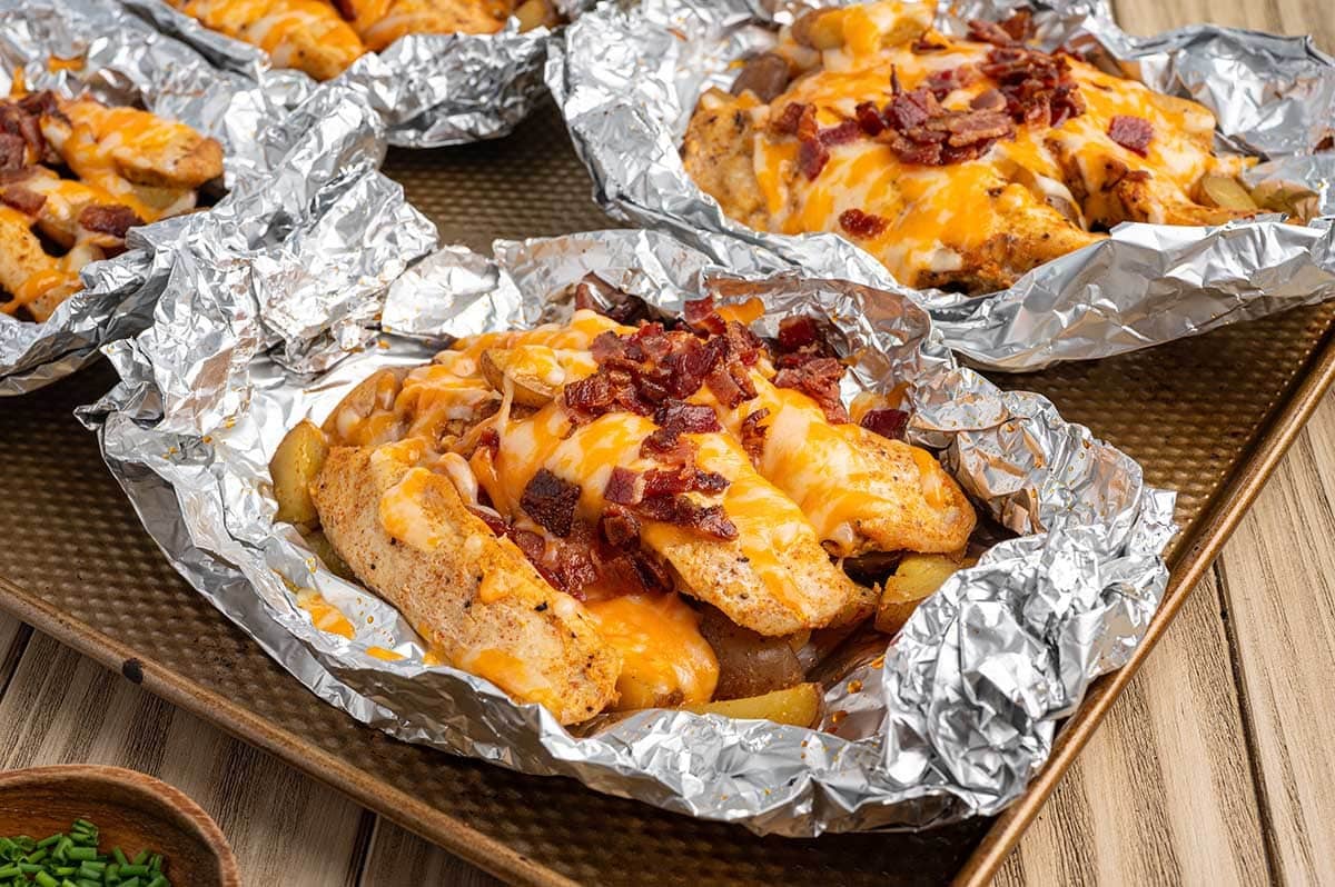 Cheesy bacon chicken foil packets with potatoes served in foil on a baking sheet.