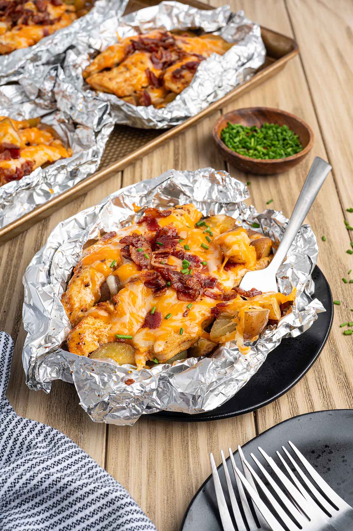 Cheesy bacon chicken foil packet served with potatoes and chives on a plate.