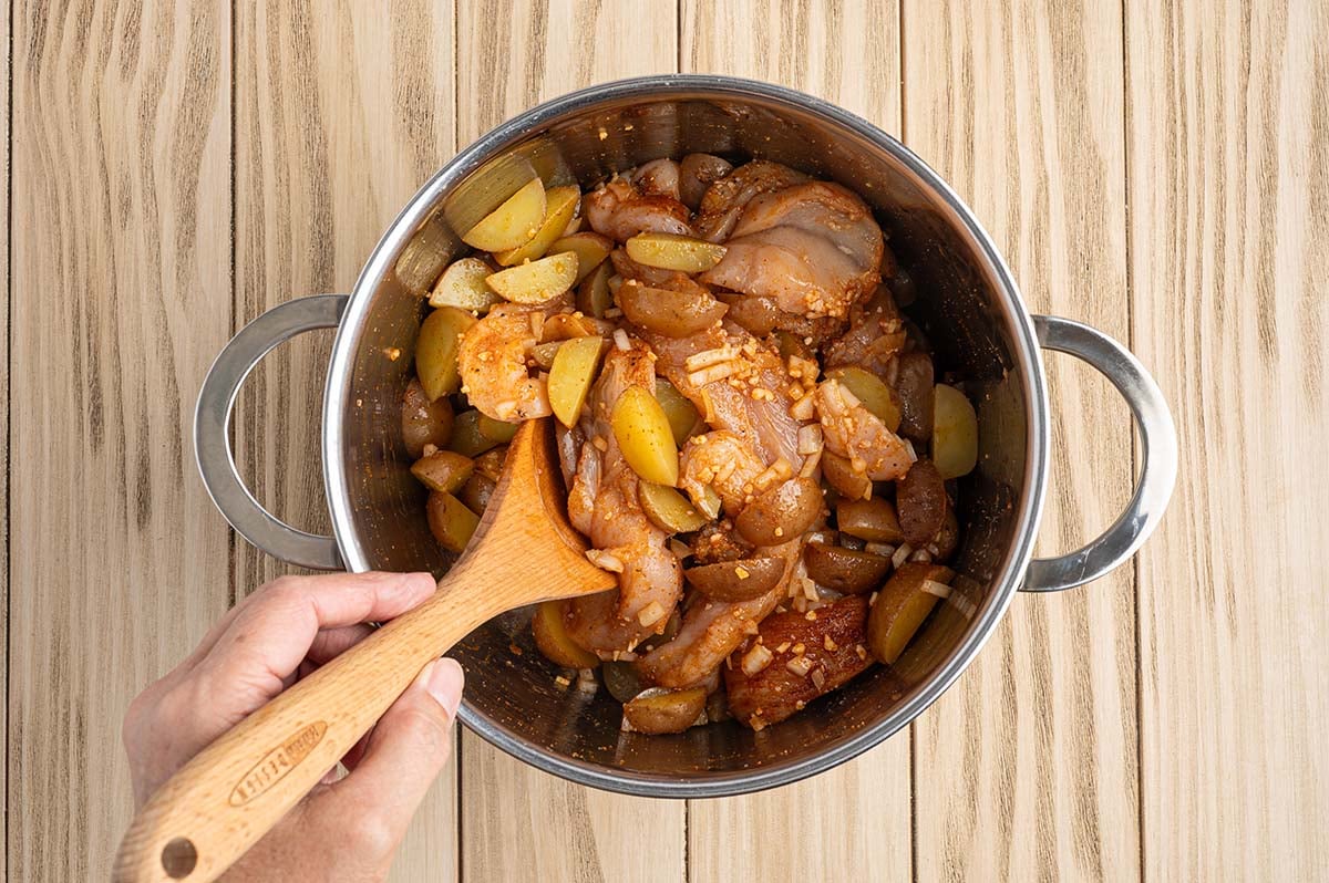 Chicken, potatoes, and onions tossed with seasonings in a pot before making foil packets.