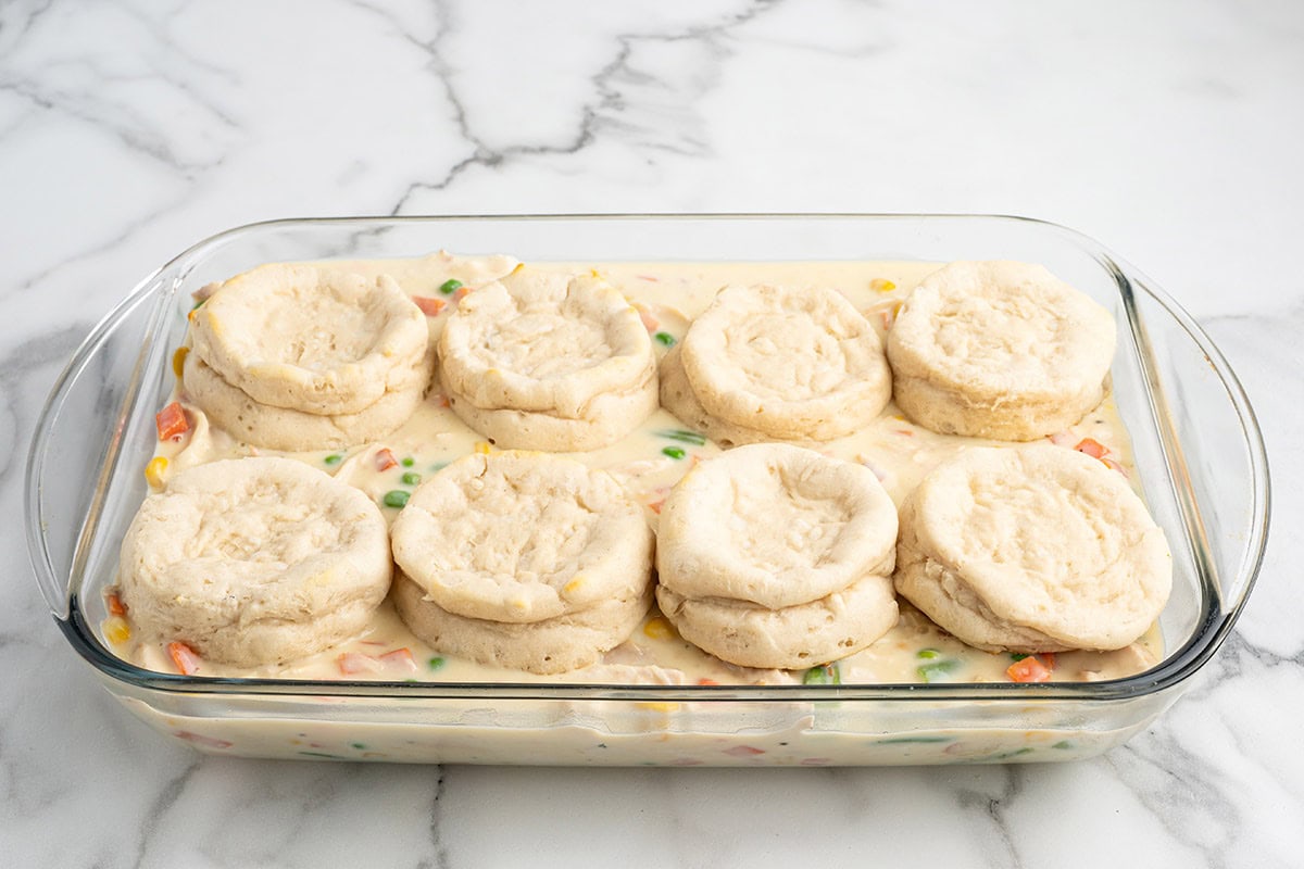 Unbaked biscuit dough arranged over chicken pot pie filling in a casserole dish.