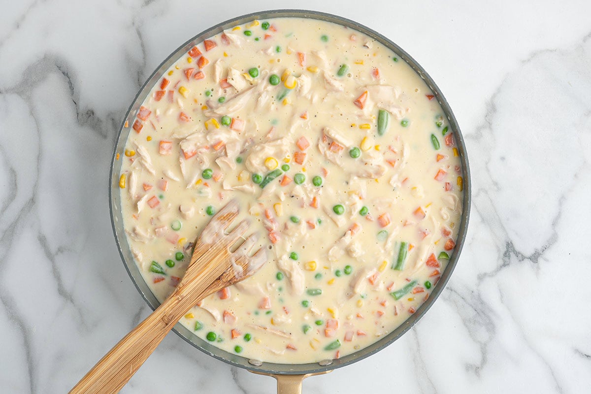 Creamy chicken and vegetable filling simmering in a skillet for pot pie casserole.