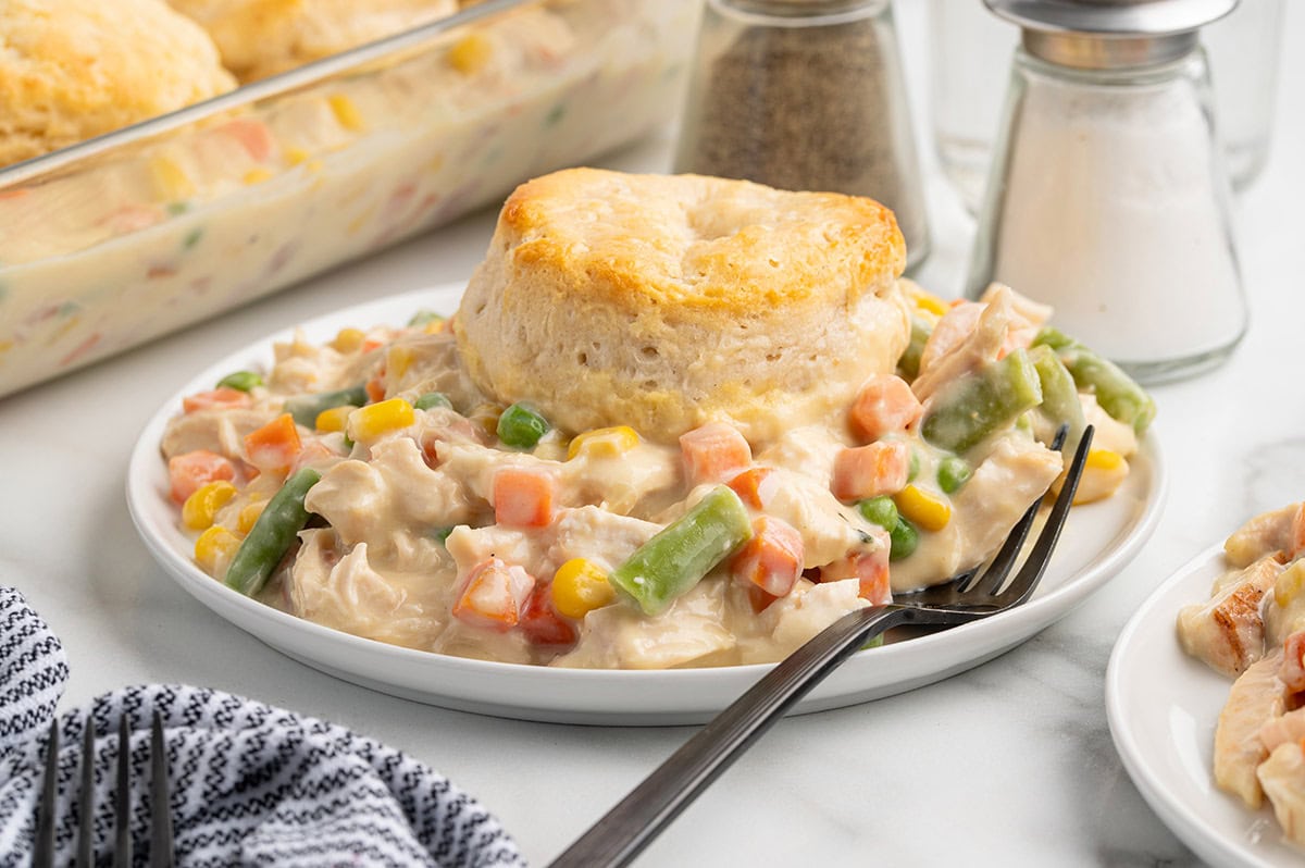 Plated serving of chicken pot pie casserole with a biscuit, vegetables, and a fork.
