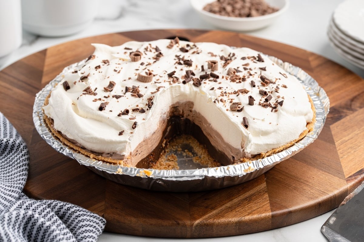 Whole layered chocolate pudding pie with a slice removed, topped with whipped cream.