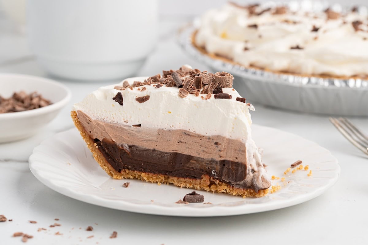 Slice of layered chocolate pudding pie on a plate with the full pie in the background.