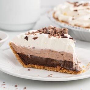 Slice of layered chocolate pudding pie topped with whipped cream and chocolate shavings.