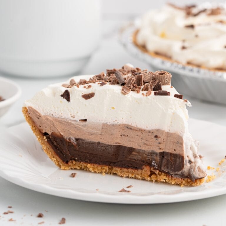 Slice of layered chocolate pudding pie topped with whipped cream and chocolate shavings.