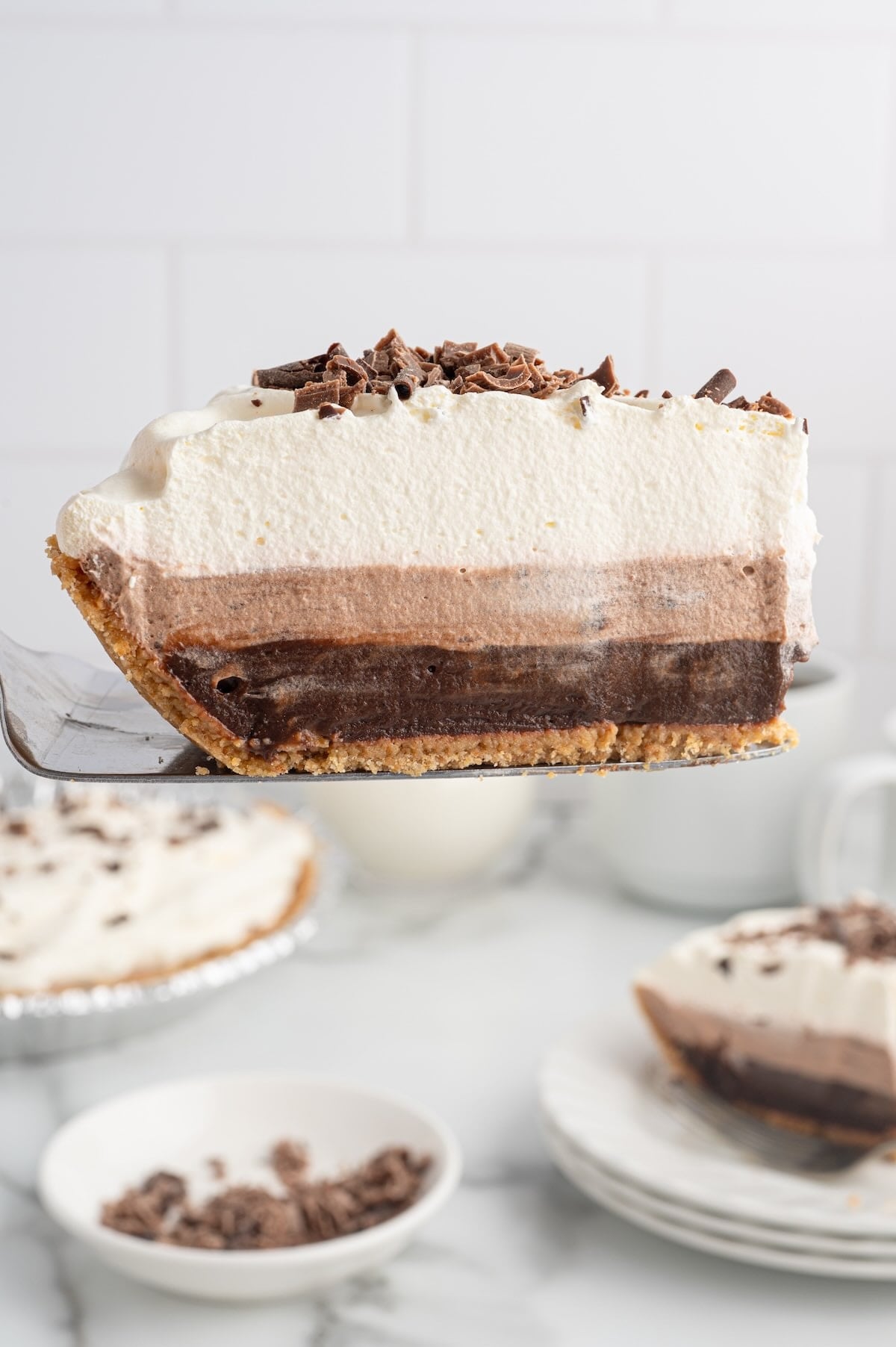 Pie server lifting a slice of layered chocolate pudding pie with chocolate shavings on top.
