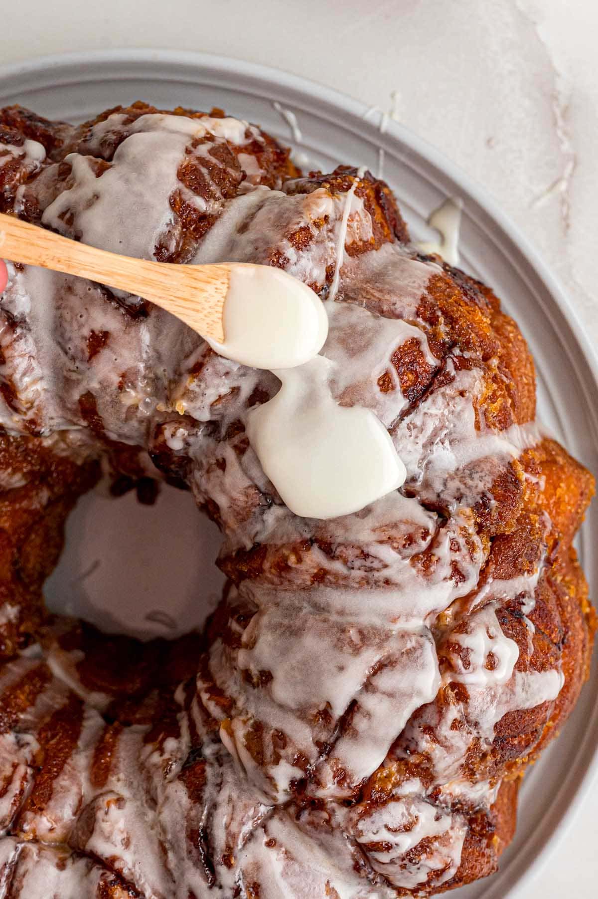 Vanilla glaze being drizzled over freshly baked cinnamon roll monkey bread.