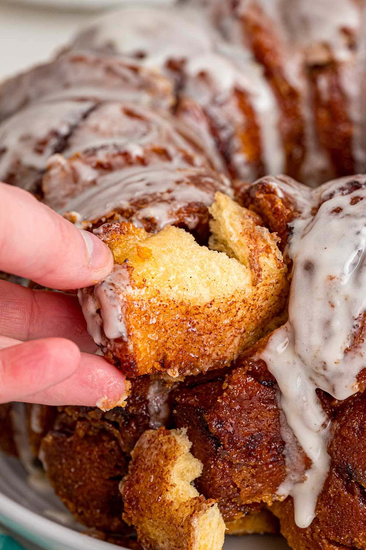 Hand pulling apart a warm, glazed piece of cinnamon roll monkey bread.