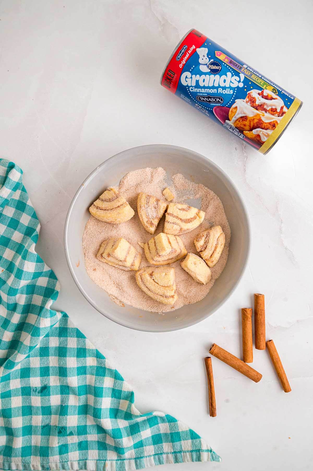 Cinnamon roll pieces coated in cinnamon sugar with a can of Pillsbury Grands cinnamon rolls nearby.