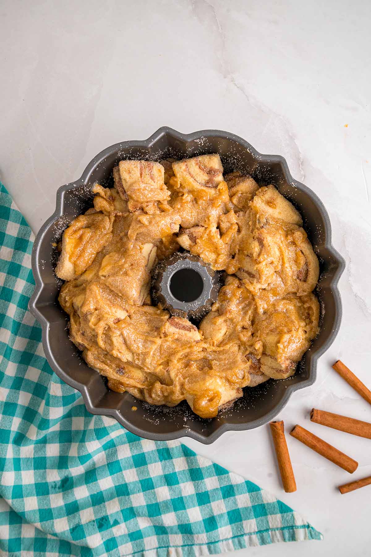 Bundt pan filled with cinnamon sugar coated cinnamon roll pieces topped with a buttery brown sugar mixture, ready to bake.