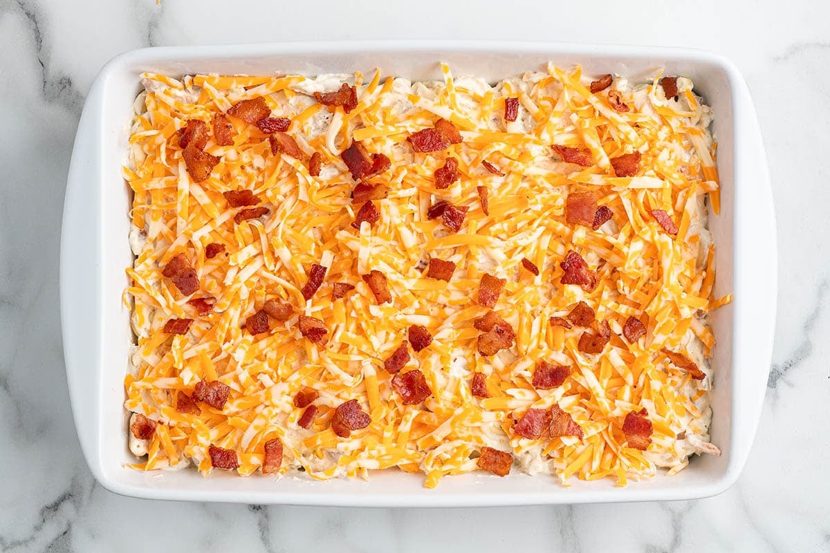 Crack chicken casserole topped with shredded cheddar and bacon before baking.