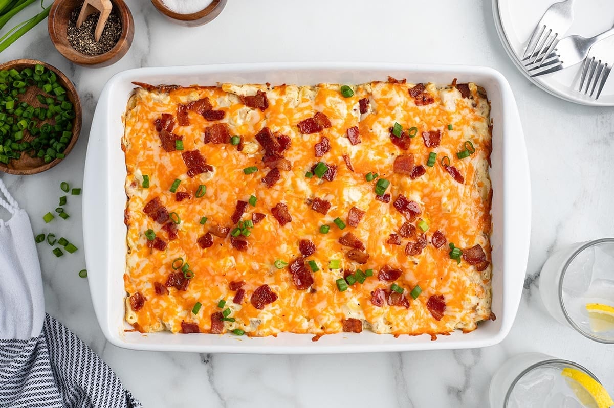"Overhead view of baked crack chicken casserole topped with cheddar cheese, bacon, and green onions.