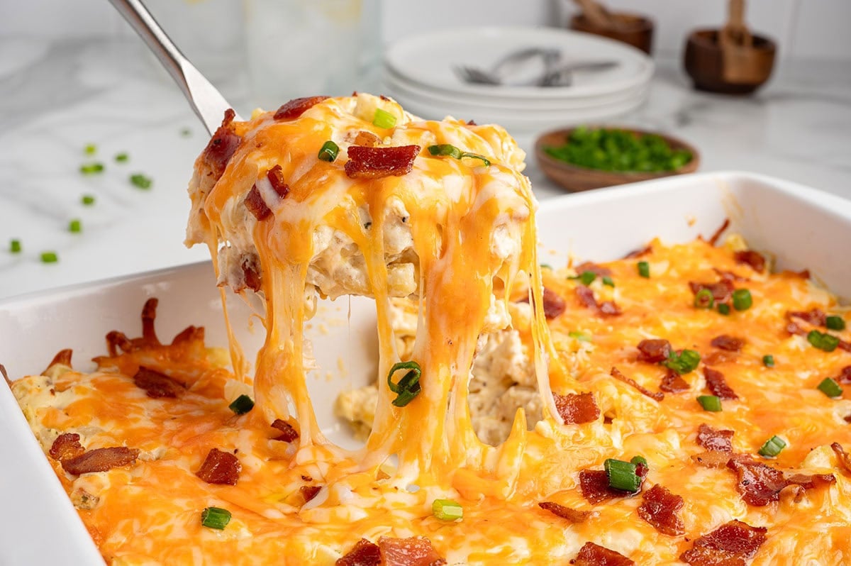 Spoon lifting a cheesy stretch of crack chicken casserole from the baking dish.