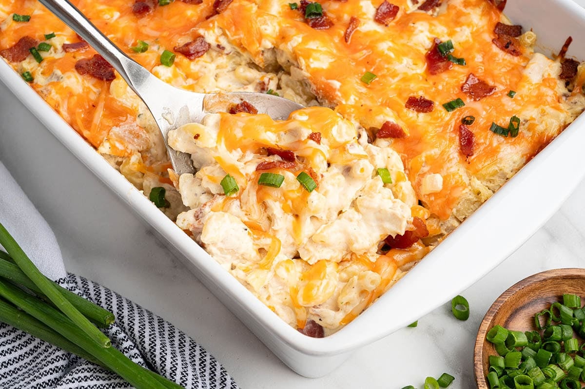 Serving spoon lifting cheesy crack chicken casserole with bacon and green onions from the dish.