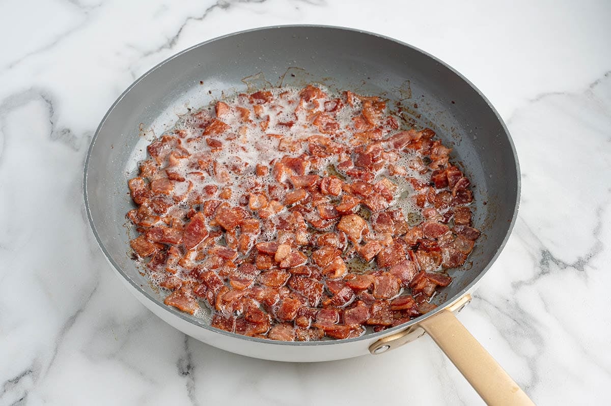 Crispy diced bacon cooking in a skillet.