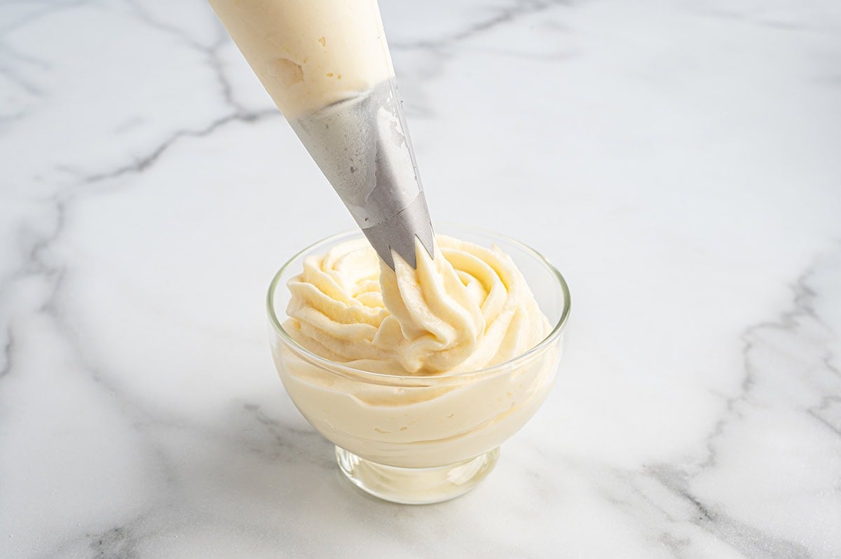 Piping bag swirling pineapple Dole Whip into a glass dish on a marble counter.