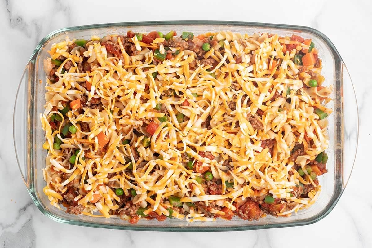 Hamburger casserole topped with shredded cheese before baking.