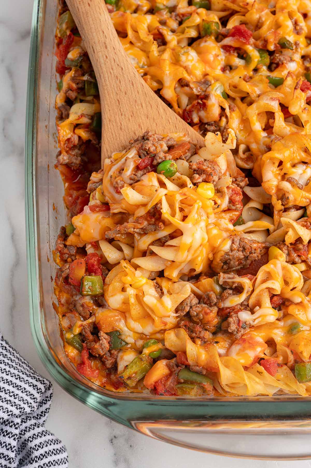 Overhead view of hamburger casserole with egg noodles, ground beef, and melted cheese being scooped with a wooden spoon.