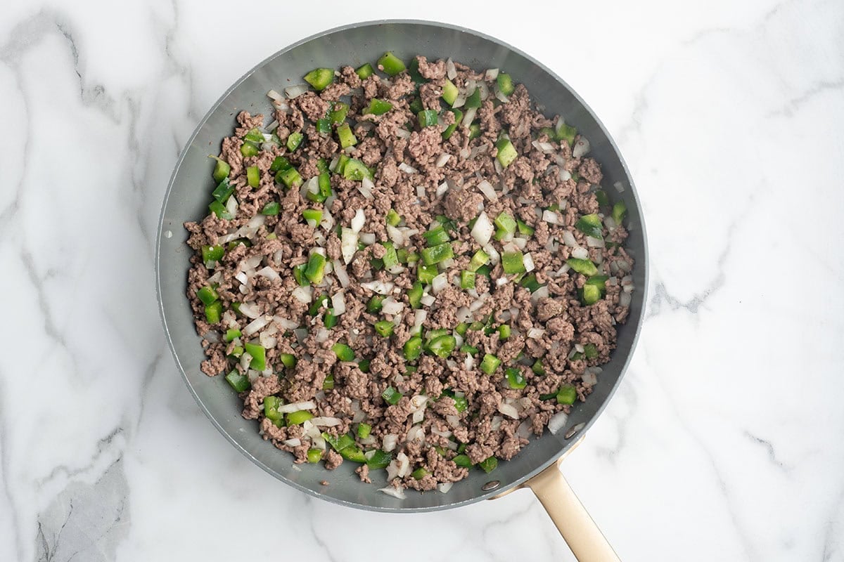 Ground beef cooking with diced onions and green peppers in a skillet.